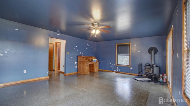 unfurnished living room with a wood stove, ceiling fan, and baseboards