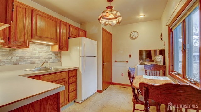 kitchen with a sink, light countertops, hanging light fixtures, freestanding refrigerator, and tasteful backsplash