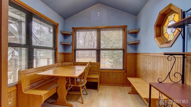 dining space with light wood finished floors, vaulted ceiling, wood walls, and wainscoting