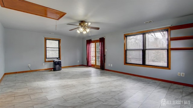 empty room with a wealth of natural light, attic access, visible vents, and baseboards