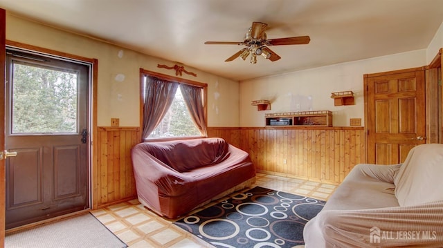 living area featuring a wainscoted wall, wooden walls, a ceiling fan, and light floors