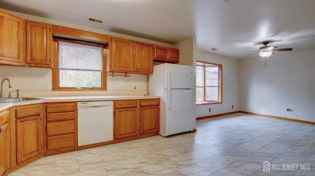 kitchen featuring light countertops, visible vents, brown cabinetry, a sink, and white appliances