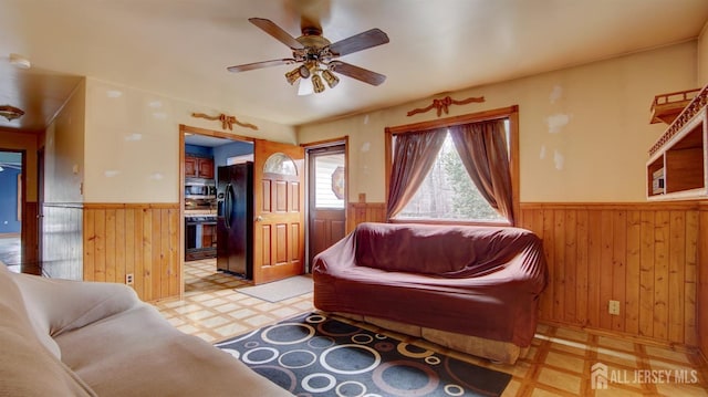 living room with a wainscoted wall, light floors, wood walls, and a ceiling fan