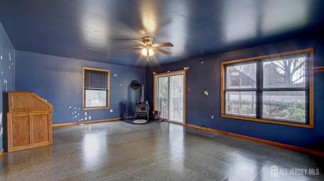 spare room with a ceiling fan, a wood stove, and baseboards