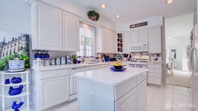 kitchen with white appliances, white cabinetry, sink, and a kitchen island