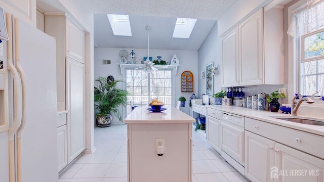 kitchen with white appliances, a skylight, a center island, sink, and light tile patterned flooring