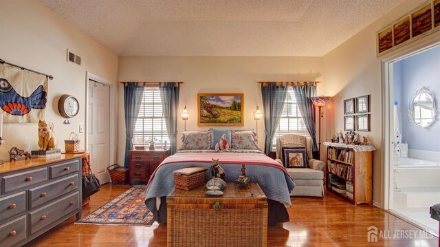 bedroom featuring a textured ceiling, light wood-type flooring, ensuite bathroom, and a closet