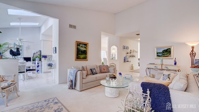 living room featuring ceiling fan, vaulted ceiling with skylight, and light colored carpet