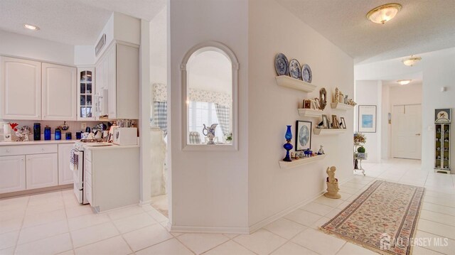 kitchen featuring a textured ceiling, white gas stove, white cabinetry, and light tile patterned floors