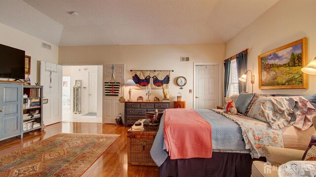 bedroom with lofted ceiling, a textured ceiling, and light hardwood / wood-style floors