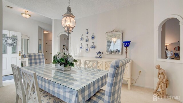 dining space with a textured ceiling and light carpet