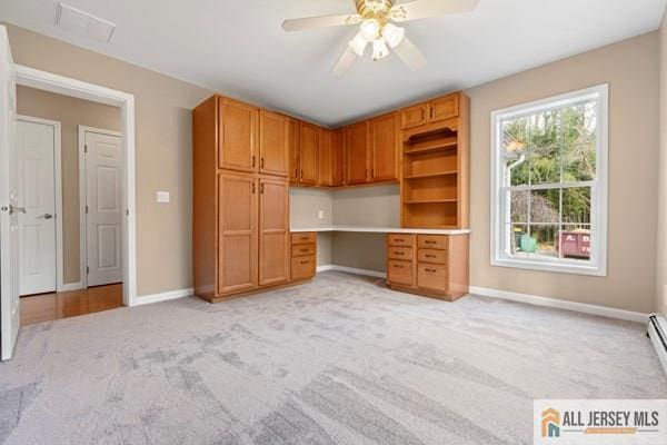 unfurnished office with built in desk, light colored carpet, and ceiling fan