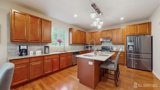 612 Magnolia Rd, North Brunswick, NJ 08902 - kitchen featuring stainless steel appliances, under cabinet range hood, light wood-style floors, decorative backsplash, and an island with sink