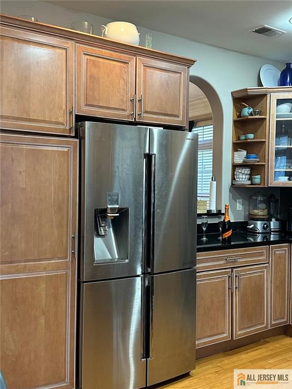 kitchen featuring open shelves, light wood-style floors, visible vents, arched walkways, and stainless steel fridge