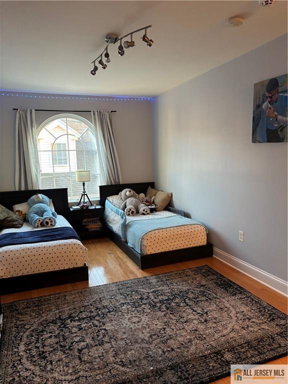 bedroom with rail lighting, wood finished floors, and baseboards