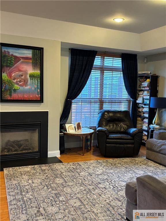 living room featuring baseboards, recessed lighting, wood finished floors, and a glass covered fireplace