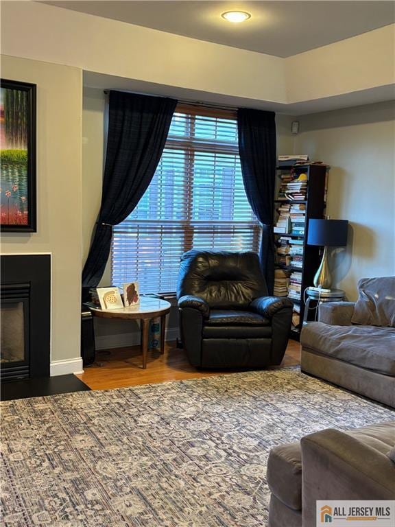 living room featuring recessed lighting, a fireplace with flush hearth, wood finished floors, and baseboards