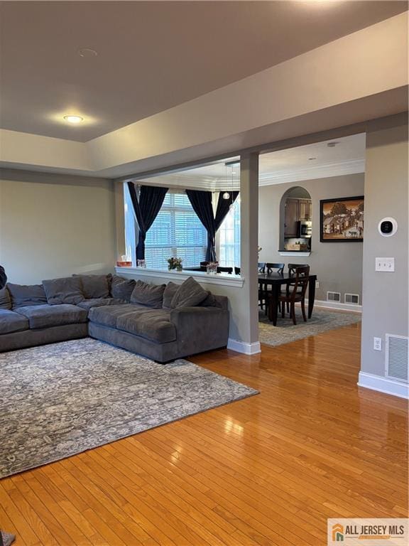 living room with visible vents, hardwood / wood-style flooring, arched walkways, and baseboards