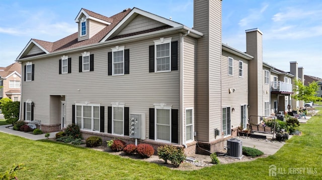 rear view of property featuring central AC unit, a lawn, brick siding, and a chimney