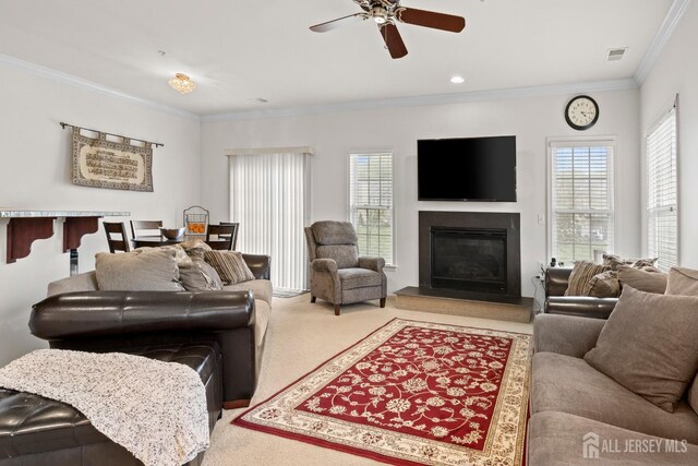 living room featuring carpet floors, ornamental molding, a glass covered fireplace, and a ceiling fan