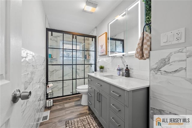 bathroom with visible vents, toilet, wood finished floors, vanity, and tile walls