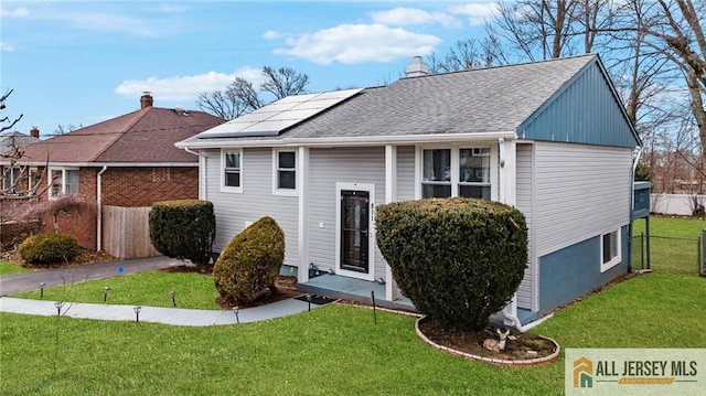 view of front of house with a shingled roof, solar panels, a chimney, fence, and a front yard