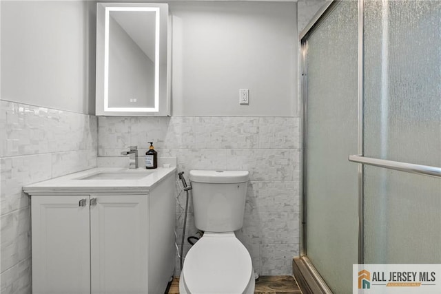 bathroom with toilet, vanity, tile walls, wainscoting, and a shower stall