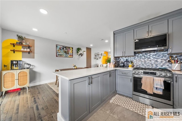 kitchen with a peninsula, light countertops, appliances with stainless steel finishes, gray cabinets, and tasteful backsplash