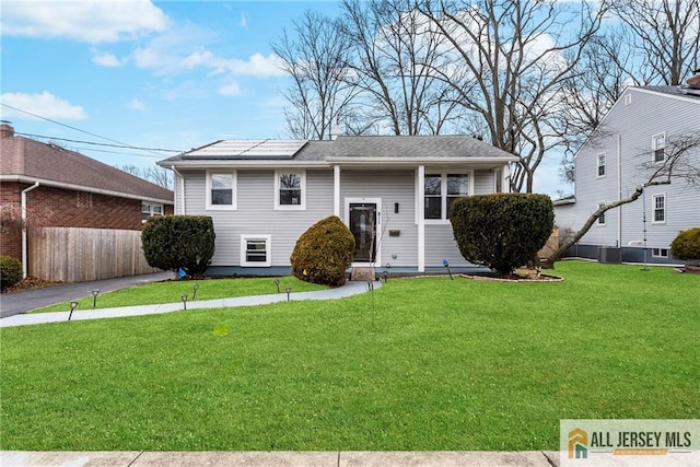 raised ranch featuring a front yard, roof mounted solar panels, cooling unit, and fence