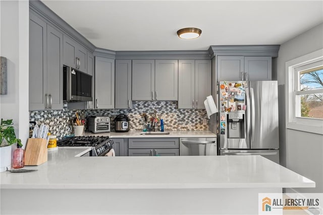 kitchen with stainless steel appliances, light countertops, backsplash, and gray cabinetry