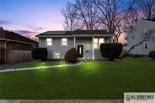 bi-level home with cooling unit, a lawn, fence, and solar panels