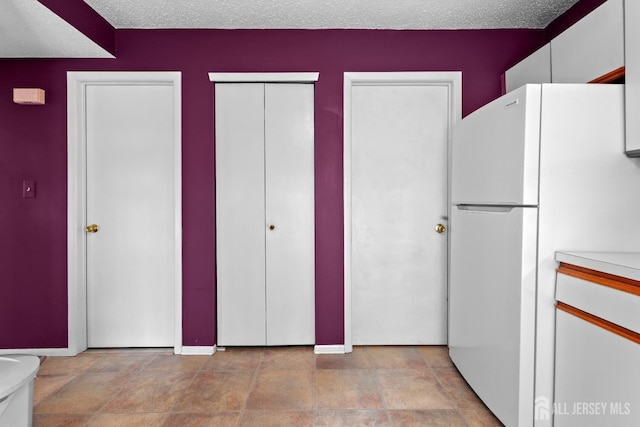 kitchen with freestanding refrigerator, light countertops, white cabinets, and baseboards