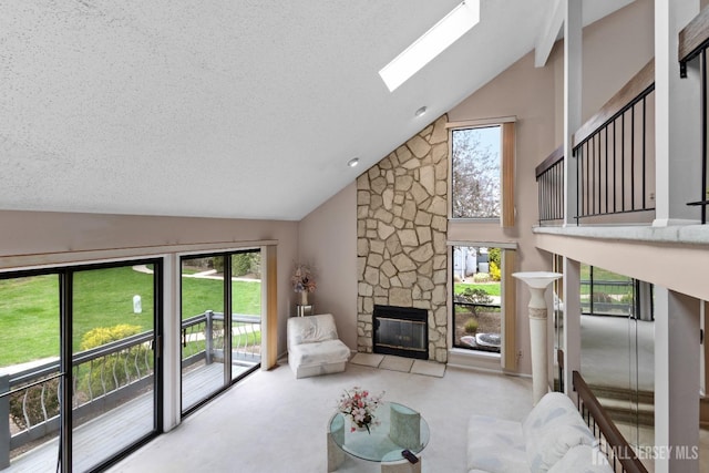 carpeted living area with a skylight, plenty of natural light, high vaulted ceiling, a stone fireplace, and a textured ceiling