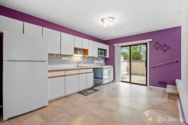 kitchen with white appliances, a sink, a textured ceiling, white cabinetry, and light countertops