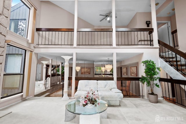 living area featuring high vaulted ceiling, plenty of natural light, ceiling fan, decorative columns, and stairway