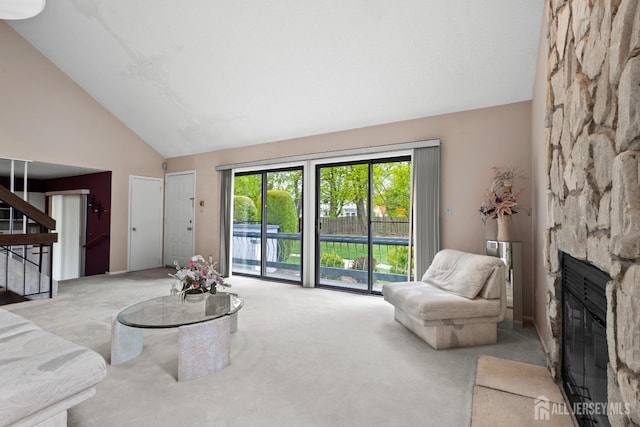 carpeted living area with stairs, a fireplace, and high vaulted ceiling