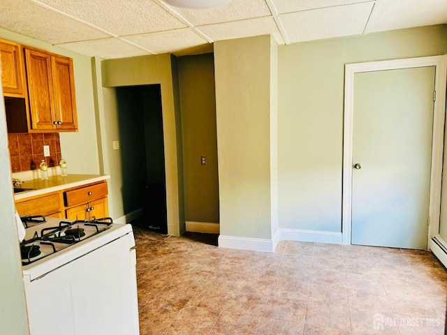 kitchen featuring light countertops, a paneled ceiling, gas range gas stove, brown cabinets, and backsplash