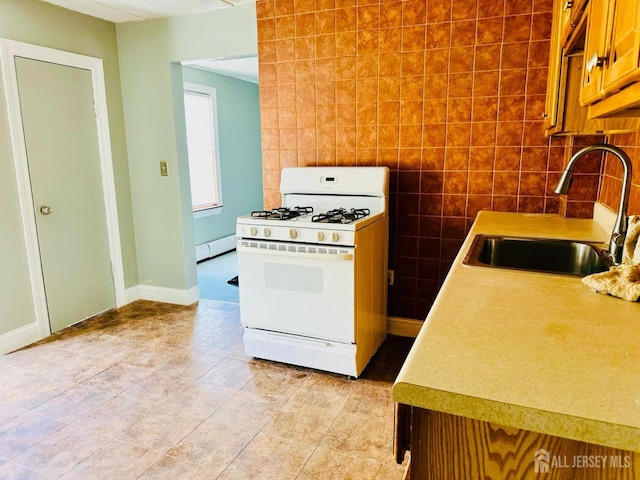 kitchen with baseboard heating, white gas range oven, light tile patterned flooring, brown cabinetry, and a sink