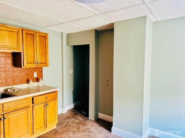 kitchen featuring baseboards, a sink, light countertops, brown cabinetry, and decorative backsplash