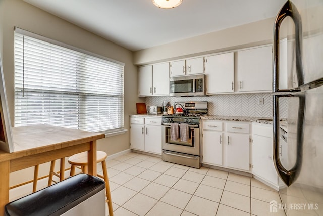 kitchen featuring white cabinetry, stainless steel appliances, light tile patterned floors, and backsplash