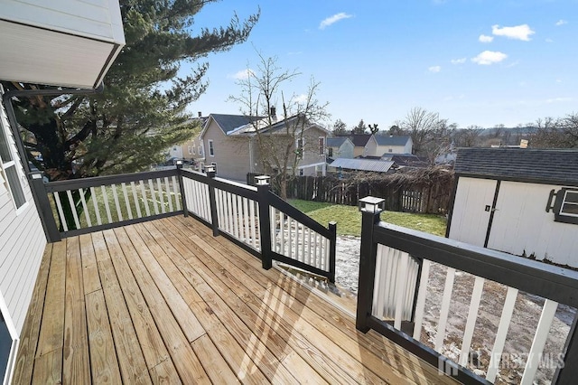 wooden terrace featuring a lawn, a fenced backyard, a residential view, an outbuilding, and a storage unit