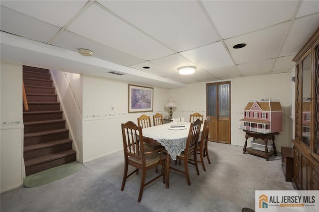 carpeted dining space with a paneled ceiling and stairs