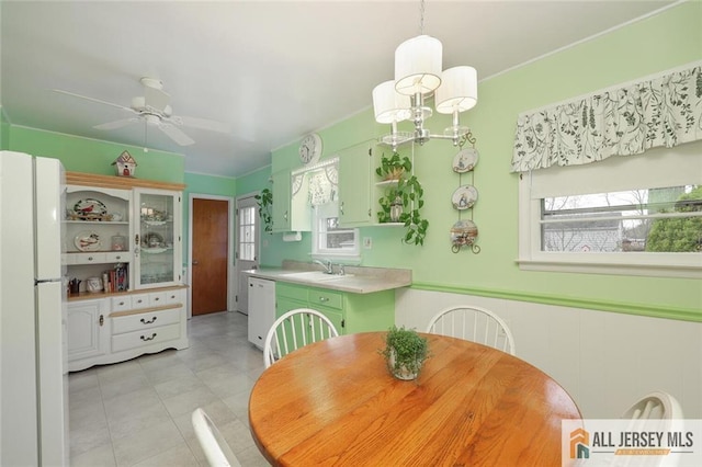 dining space with plenty of natural light, a ceiling fan, a wainscoted wall, light tile patterned floors, and a chandelier