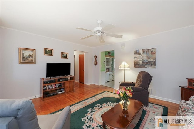 living area with wood finished floors, ceiling fan, baseboards, and crown molding