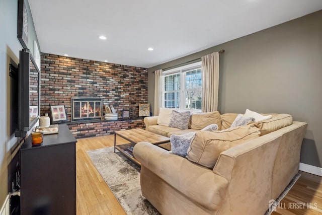 living area with brick wall, a fireplace, recessed lighting, and wood finished floors
