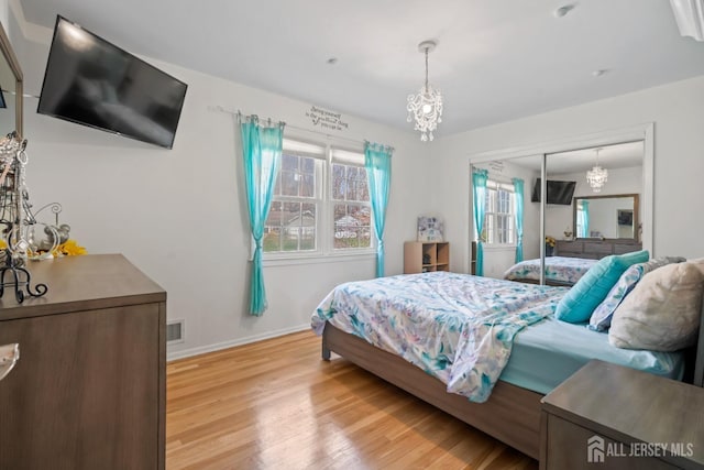 bedroom featuring an inviting chandelier, light wood finished floors, baseboards, visible vents, and a closet
