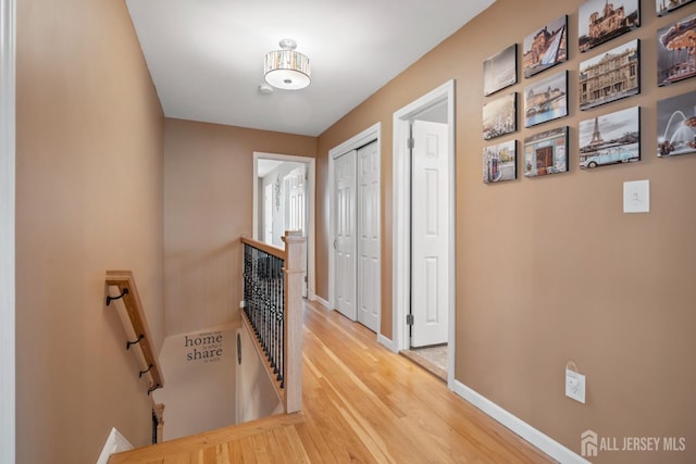 hall with baseboards, light wood finished floors, and an upstairs landing