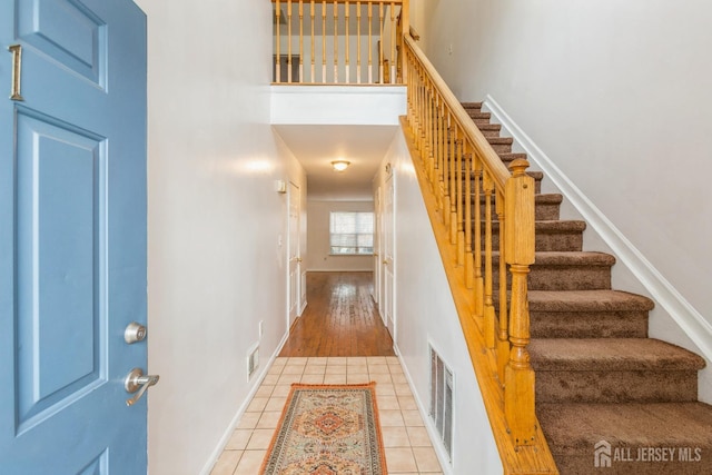 stairway featuring tile patterned floors, baseboards, visible vents, and a towering ceiling