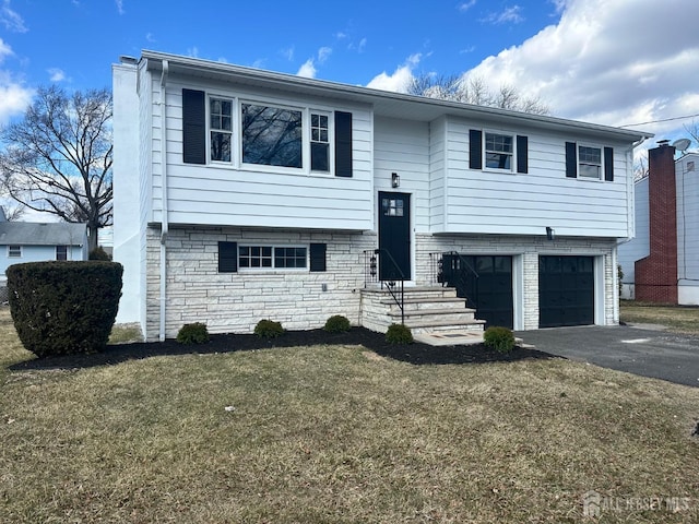 bi-level home with a front yard, a garage, stone siding, and driveway