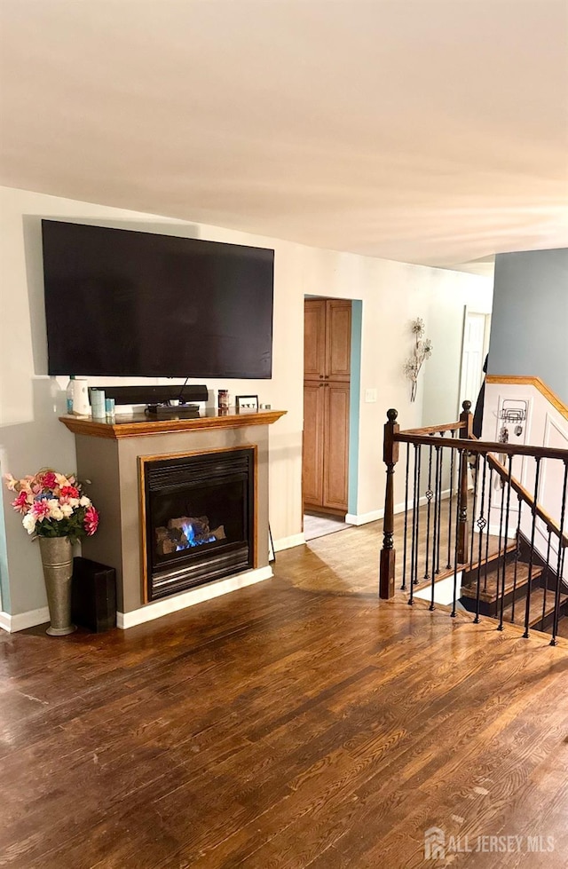 living room with stairs, a glass covered fireplace, baseboards, and wood finished floors